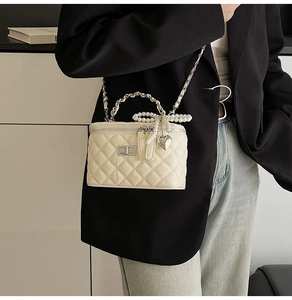 Detail of white quilted chain bag with pearl bow and silver heart charm on model