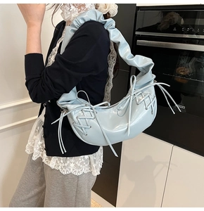 Détail du sac demi-lune en cuir verni bleu clair avec lacets corset et nœud sur la bandoulière