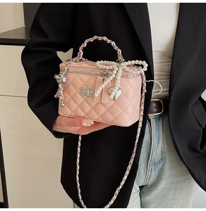Detail of pink quilted handbag with pearl bow charm and chain handle worn by a model
