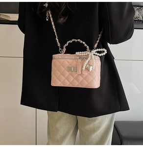 Detail of pink quilted chain bag with pearl bow and heart charm on black blazer