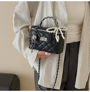 Detail of black quilted box bag featuring silver chain and pearl bow charm detail