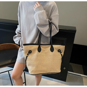 Detail of the woven texture and black leather straps on the large straw tote bag