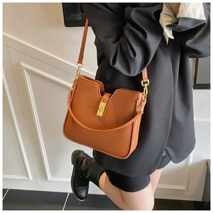 Detail of a brown leather bag with a U-shaped opening and golden rotating metal clasp