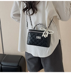 Detail of black quilted leather crossbody bag with pearl bow and metal chain strap