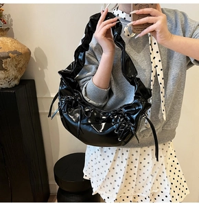 Détail d'un sac demi-lune en cuir verni noir brillant avec poignée plissée et laçage