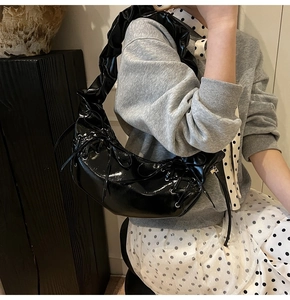 Détail du sac demi-lune en cuir verni noir avec bandoulière plissée et nœuds déco
