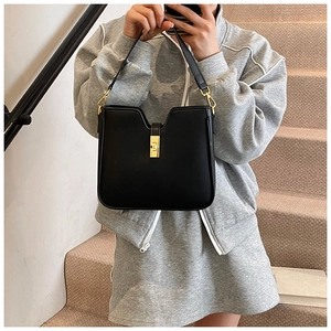 Close-up of minimalist black leather shoulder bag with a sleek rectangular gold metal lock