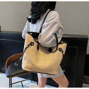 Detail of a large woven straw tote bag with black leather straps and gold metal rings