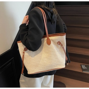 Model wearing a large cream woven tote bag with brown leather trim on wooden stairs