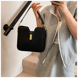 Detail of a chic black bucket bag with gold clasp held by a model on stairs