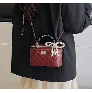 Detail of wine red quilted bag with pearl bow charm and silver chain strap