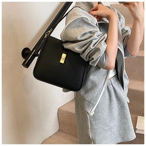 Detail of a black leather bucket bag with a golden twist-lock buckle and smooth finish