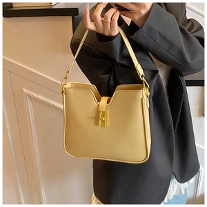 Detail of a creamy yellow leather bucket bag featuring a golden twist lock and concave topline