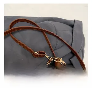 Detail of adjustable brown shoulder strap with gold metal buckle and plush ball charm