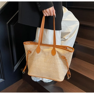 Detail of woven straw tote bag featuring brown faux leather handles and metal hardware