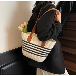 Détail d'un grand sac cabas tissé avec rayures noires et fines anses en cuir marron