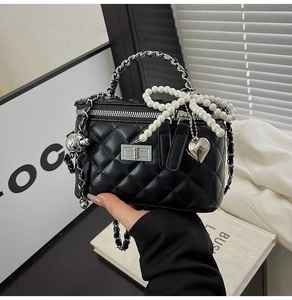 Detail of black quilted leather vanity bag with silver chain handle and pearl bow charm