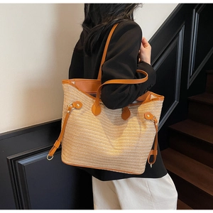 Detail of straw tote bag with brown leather handles and metallic rivets worn by model