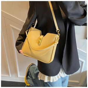 Detail view of a creamy yellow U-shaped bag with a golden square twist lock on a black suit