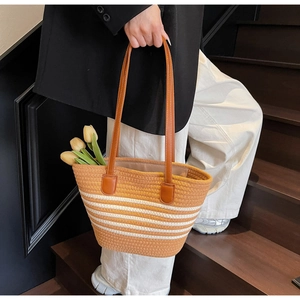 Détail d'un grand sac cabas tressé avec rayures blanches et anses en cuir marron