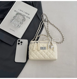 Detail of cream quilted handbag with pearl bow and heart charm on silver chain strap