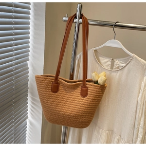 Detail of ginger woven tote bag with tulip ornament and brown leather straps on a hanger
