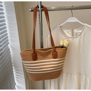 Detail of woven tote bag with white stripes and brown leather straps on a hanger