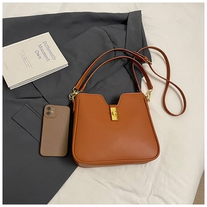 Detail of caramel leather shoulder bag featuring a gold metal twist lock and adjustable strap