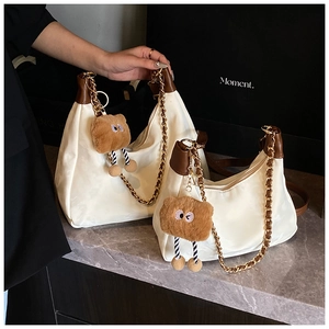 Close-up of beige tote bags with dark brown trim, metal chains and plush bear charms