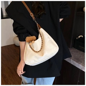 Close-up of white hobo bag with brown strap and gold chain worn by a person in black suit