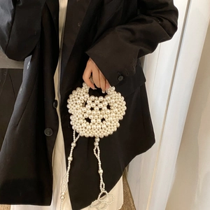 Detail of handcrafted white pearl woven round handbag held against black blazer backdrop