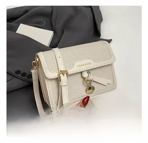 Detail of cream woven shoulder bag with gold buckle closure and round metal pendant
