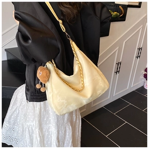 Detail of cream hobo bag featuring gold chain strap and a cute bear plush pendant