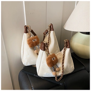 Detail view of two white matte PU leather hobo bags with brown plush monster charms