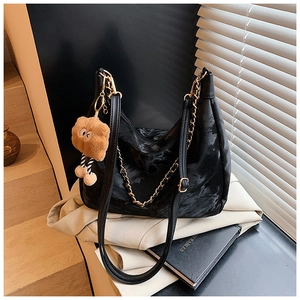 Detail of black tote bag with gold chain strap and cute brown teddy bear keychain charm