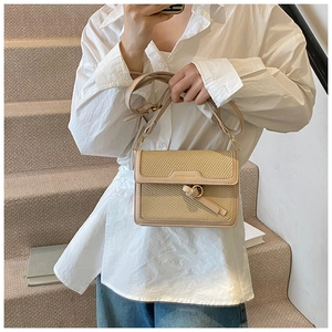 Close-up of woven cream shoulder bag featuring gold hardware and contrast leather trim