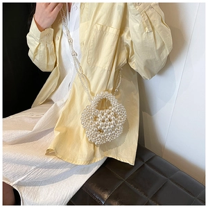 Detail of hand-woven cream white pearl crossbody bag worn over a soft yellow shirt