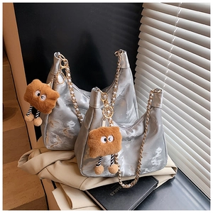 Close-up of silver textured tote bags with golden chains and plush charm on a desk