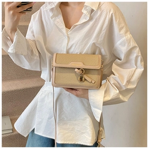 Detail of minimalist straw crossbody bag with leather trim and decorative tassel