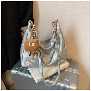 Detail of silver metallic tote bag featuring gold chain and plush brown charm accessory