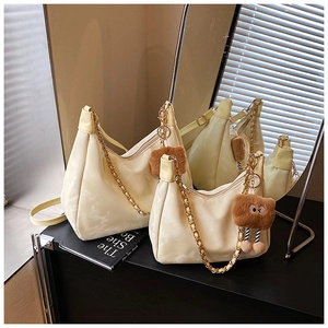 Detail of cream hobo bag with gold chain strap, plush pendant, and dual straps design