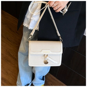 Macro shot of a cream square bag featuring twill texture and gold ring charm detail