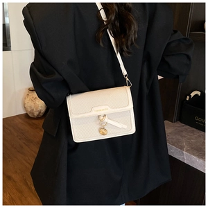 Detail of cream crossbody bag featuring woven texture and gold circular charm pendant