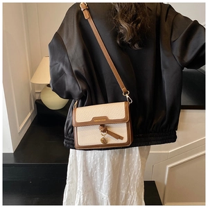 Detail of woven beige crossbody bag with brown leather trim and metallic pendant charm