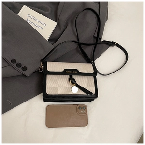 Detail of a chic beige woven crossbody bag with black leather trim and smartphone for scale