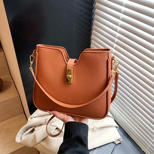 Caramel U-shaped tote bag with gold twist lock and adjustable strap in urban setting