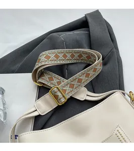 Detail of embroidered geometric wide strap and gold hardware on cream leather bucket bag