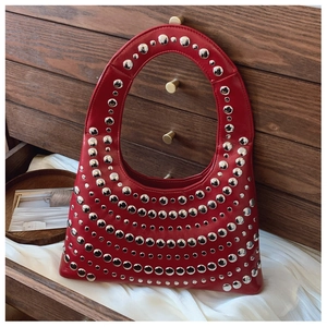 Detail der dunkelroten Ledertasche mit silbernen Metallnieten auf dunklem Holzhintergrund