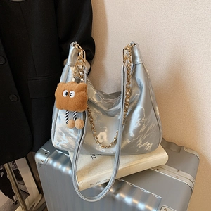 Silver metallic hobo bag with gold chain and plush charm on a silver suitcase