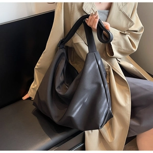 Detailed view of black large capacity soft leather tote bag worn by a model in a trench coat